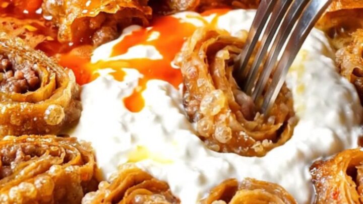 Beyti kebab pinwheels arranged in a circle around garlic yogurt, with tomato butter being poured over