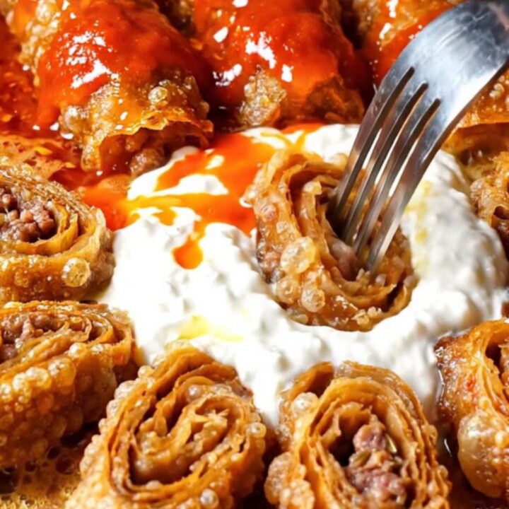 Beyti kebab pinwheels arranged in a circle around garlic yogurt, with tomato butter being poured over