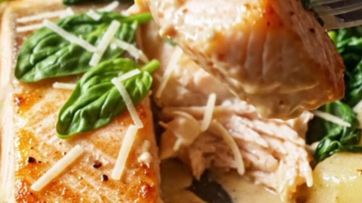 Crispy-skinned salmon fillet resting in a creamy sun-dried tomato sauce with golden gnocchi and wilted spinach in a skillet