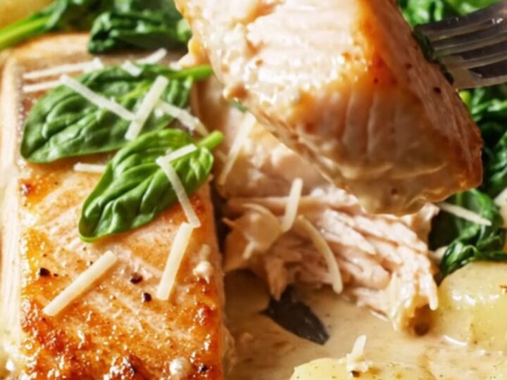 Crispy-skinned salmon fillet resting in a creamy sun-dried tomato sauce with golden gnocchi and wilted spinach in a skillet