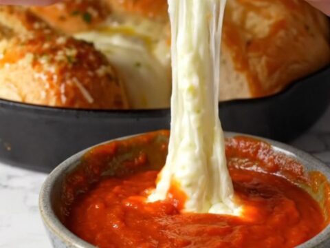 Golden pull-apart brioche rolls with melted mozzarella stretching between them, in a cast-iron skillet