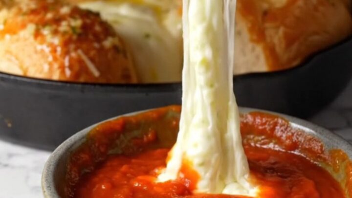Golden pull-apart brioche rolls with melted mozzarella stretching between them, in a cast-iron skillet