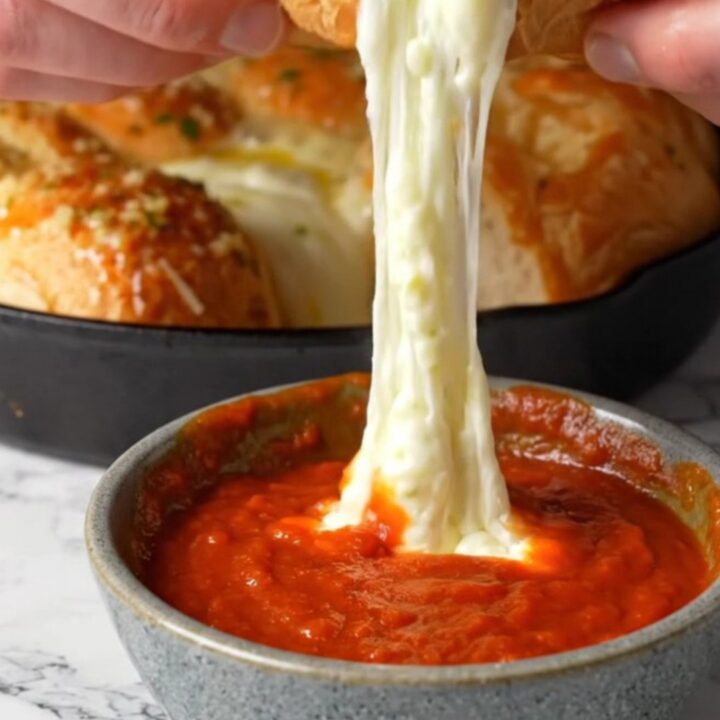 Golden pull-apart brioche rolls with melted mozzarella stretching between them, in a cast-iron skillet