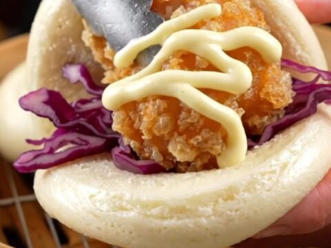 A soft steamed bao bun filled with golden crispy chicken karaage, purple cabbage, and a zigzag of Kewpie mayo.