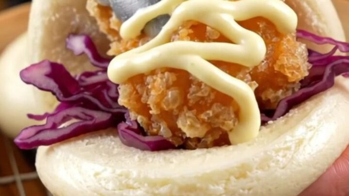 A soft steamed bao bun filled with golden crispy chicken karaage, purple cabbage, and a zigzag of Kewpie mayo.