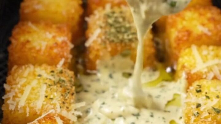 Golden crispy parmesan polenta bites on a plate with a bowl of garlic herb aioli for dipping