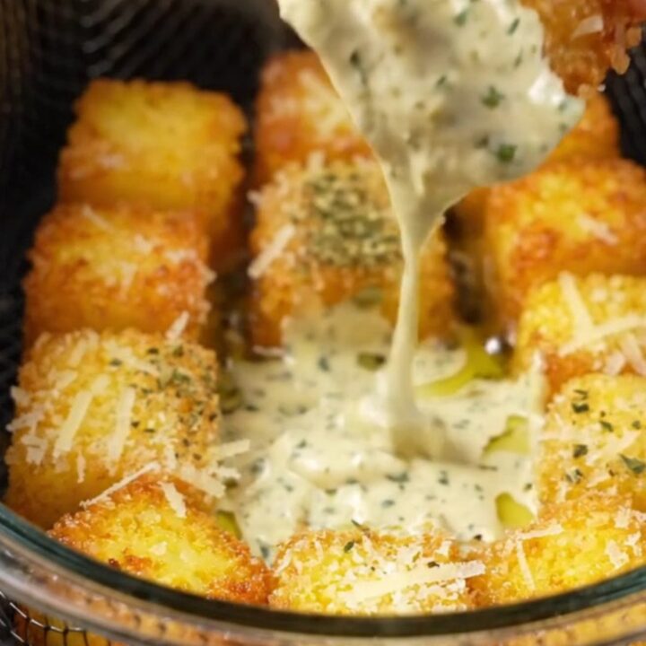 Golden crispy parmesan polenta bites on a plate with a bowl of garlic herb aioli for dipping