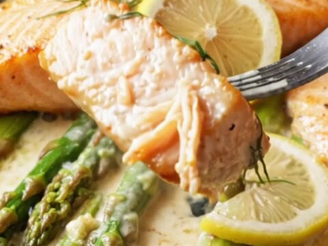 Pan-seared salmon fillets with crisp golden skin, nestled in a creamy lemon garlic caper sauce with bright green asparagus