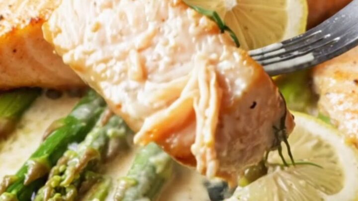 Pan-seared salmon fillets with crisp golden skin, nestled in a creamy lemon garlic caper sauce with bright green asparagus