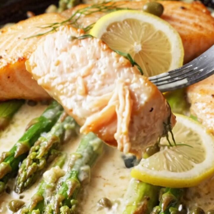 Pan-seared salmon fillets with crisp golden skin, nestled in a creamy lemon garlic caper sauce with bright green asparagus