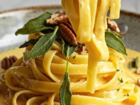 A plate of creamy butternut squash fettuccine topped with crispy sage and toasted pecans.