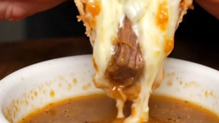 A slice of birria stuffed crust pizza being pulled, with melted cheese stretching and the crust broken to show the molten