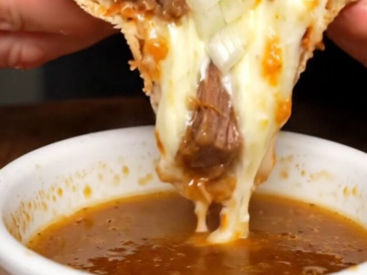A slice of birria stuffed crust pizza being pulled, with melted cheese stretching and the crust broken to show the molten