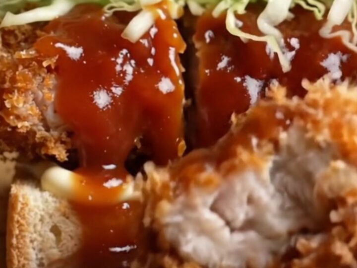 A chicken katsu sando cut in half, showing crispy golden chicken, shredded cabbage, and tonkatsu sauce on soft white bread.