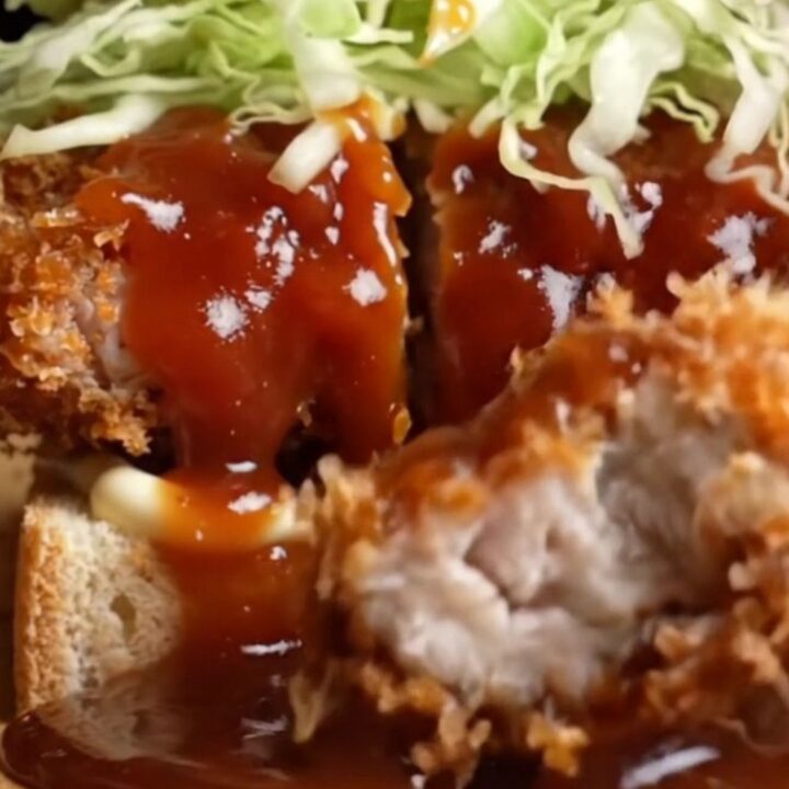 A chicken katsu sando cut in half, showing crispy golden chicken, shredded cabbage, and tonkatsu sauce on soft white bread.