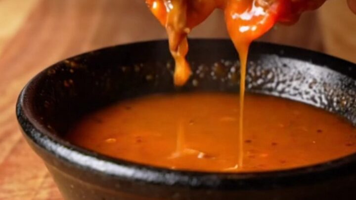 Crispy birria mulitas sliced in half, showing layers of beef and melted cheese, with a bowl of consommé for dipping