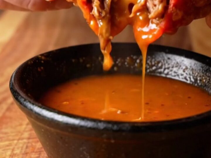 Crispy birria mulitas sliced in half, showing layers of beef and melted cheese, with a bowl of consommé for dipping