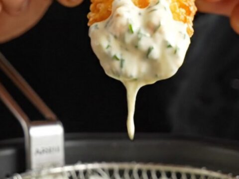 Crispy accordion zucchini fries with golden edges, served with a bowl of creamy herb aioli.