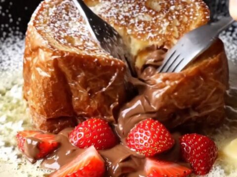 Giant stuffed Nutella brioche French toast cut open showing molten Nutella and strawberries
