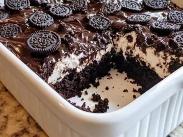 Oreo Earthquake Cake in a white ceramic dish topped with glossy fudge and crushed cookies.