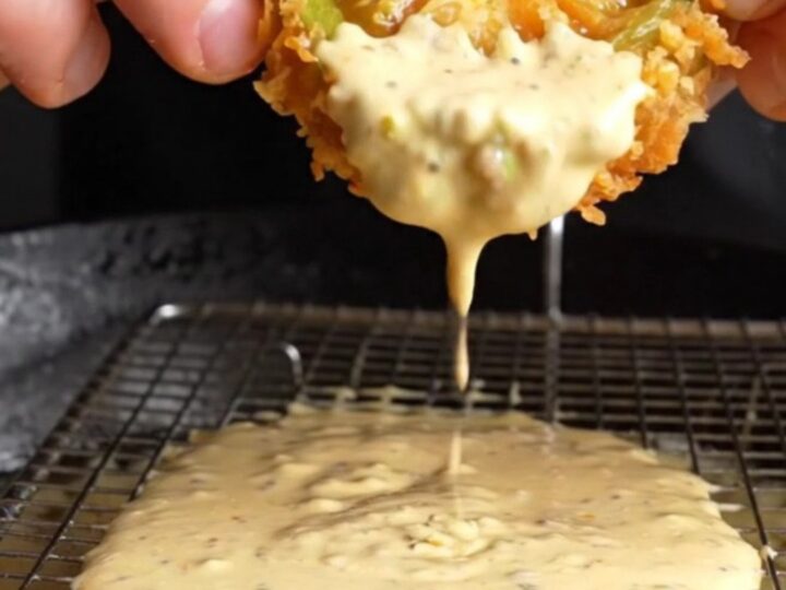 Golden fried green tomato slices with a crispy panko crust, served with a bowl of remoulade sauce on a rustic plate.