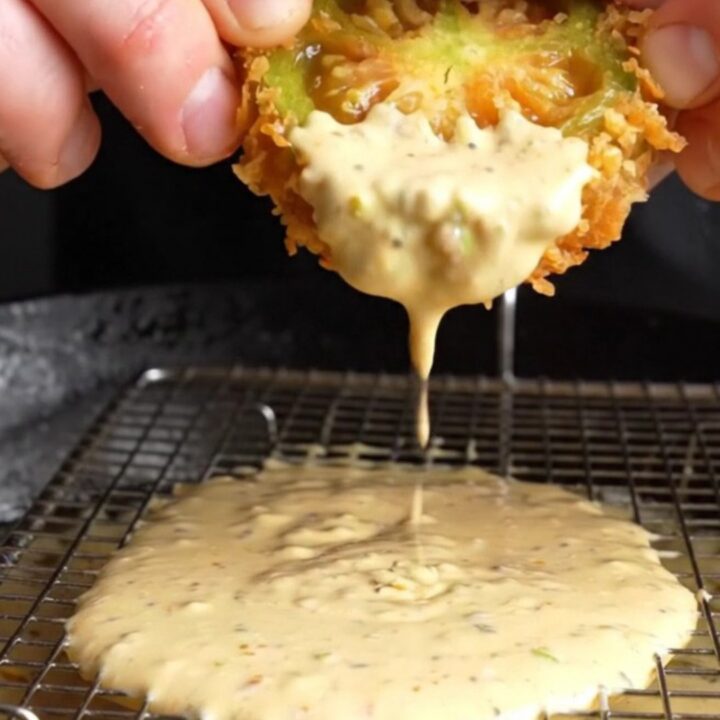 Golden fried green tomato slices with a crispy panko crust, served with a bowl of remoulade sauce on a rustic plate.