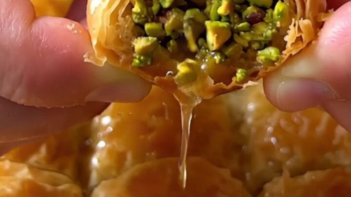 Golden pistachio rolled baklava fingers on a serving platter, drizzled with syrup and sprinkled with ground pistachios