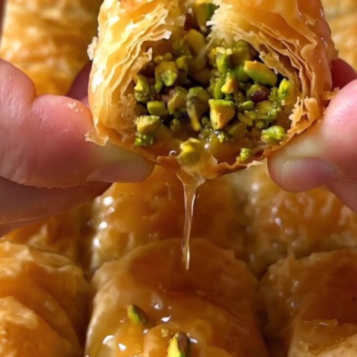Golden pistachio rolled baklava fingers on a serving platter, drizzled with syrup and sprinkled with ground pistachios