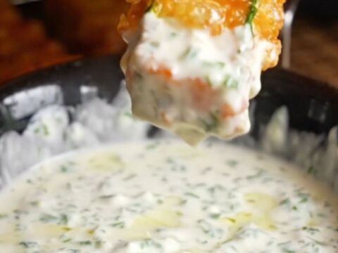 Golden accordion zucchini fries on a platter with a bowl of herb yogurt dip