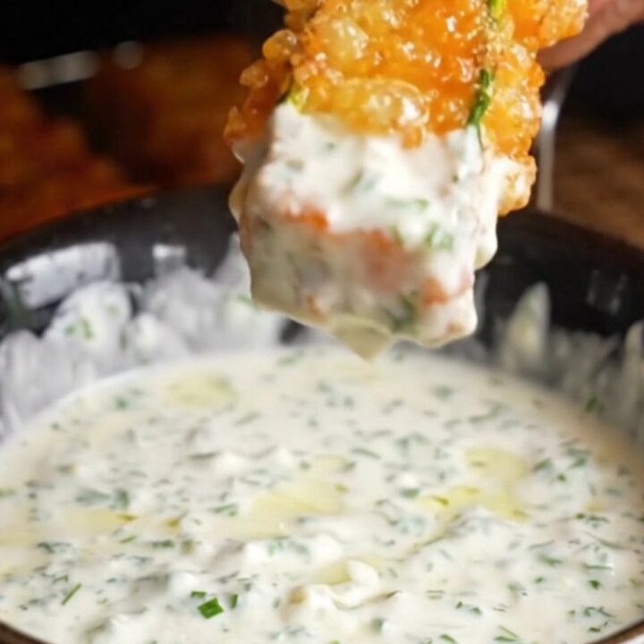 Golden accordion zucchini fries on a platter with a bowl of herb yogurt dip