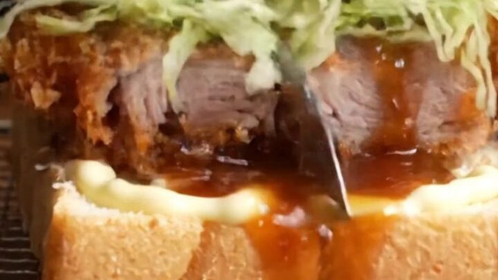 A towering tonkatsu sandwich with crispy pork cutlet, cabbage, and sauce between milk bread
