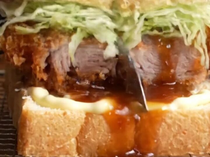 A towering tonkatsu sandwich with crispy pork cutlet, cabbage, and sauce between milk bread
