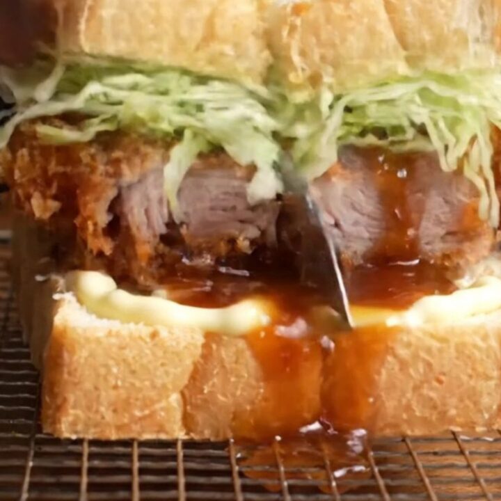 A towering tonkatsu sandwich with crispy pork cutlet, cabbage, and sauce between milk bread