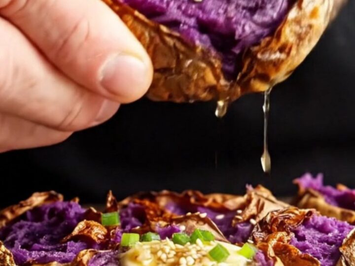 Crispy smashed purple sweet potatoes with melted miso butter, sesame seeds, and scallions on a baking sheet.