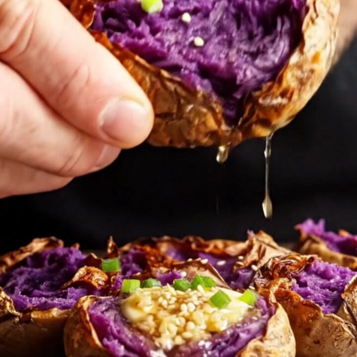 Crispy smashed purple sweet potatoes with melted miso butter, sesame seeds, and scallions on a baking sheet.