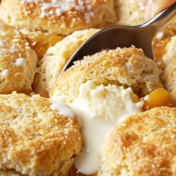 Cast iron skillet with golden buttermilk biscuits over bubbling peach filling