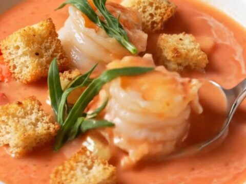 A bowl of creamy coral-pink lobster bisque topped with lobster medallions and garlic croutons, garnished with fresh tarragon.