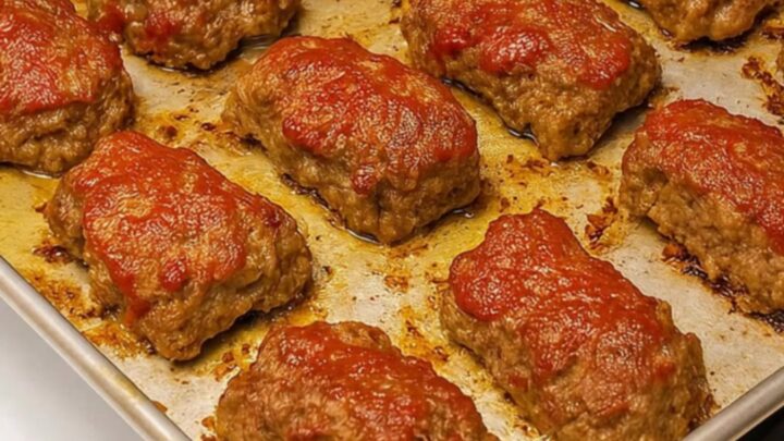 A close-up of a perfectly baked mini meatloaf on a metal tray with a glistening, caramelized red glaze.