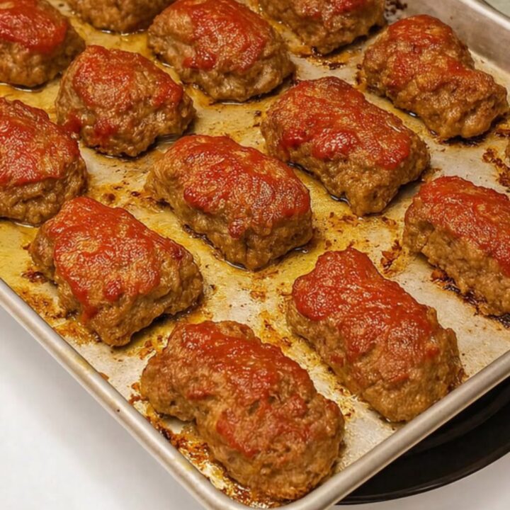 A close-up of a perfectly baked mini meatloaf on a metal tray with a glistening, caramelized red glaze.