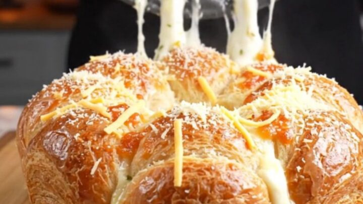 Golden brown pull-apart crown on a wooden board with melted cheese stretching between pieces