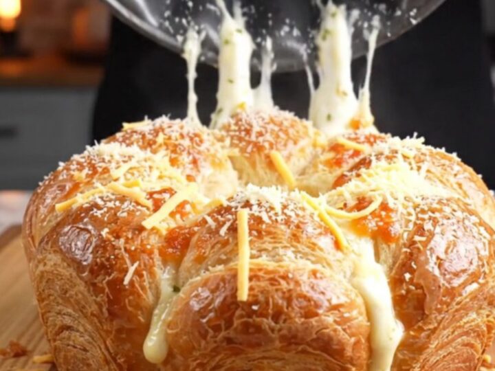 Golden brown pull-apart crown on a wooden board with melted cheese stretching between pieces