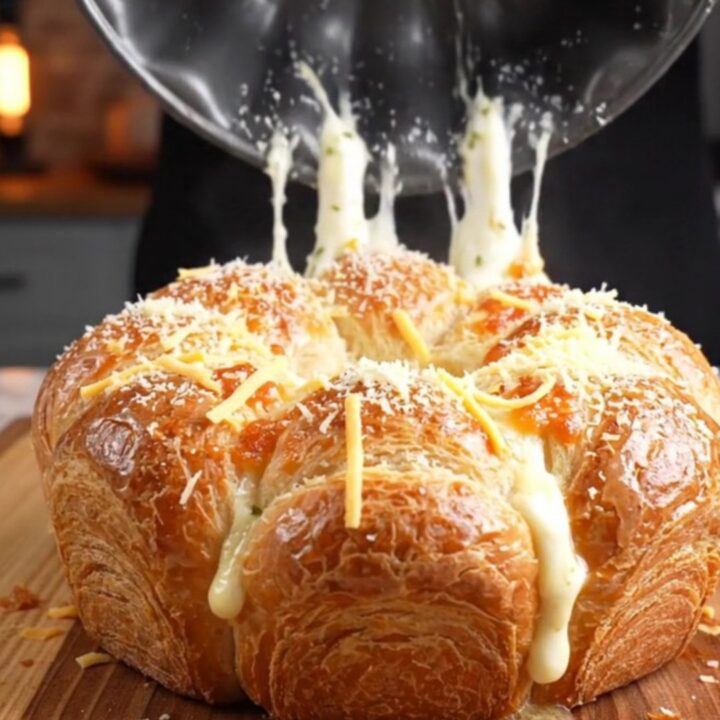 Golden brown pull-apart crown on a wooden board with melted cheese stretching between pieces