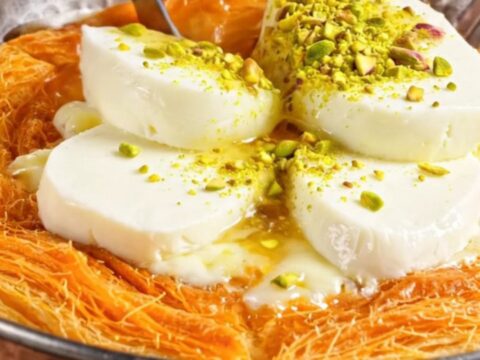 Freshly cooked pistachio kunefe in a copper pan, topped with ground pistachios and a glossy syrup