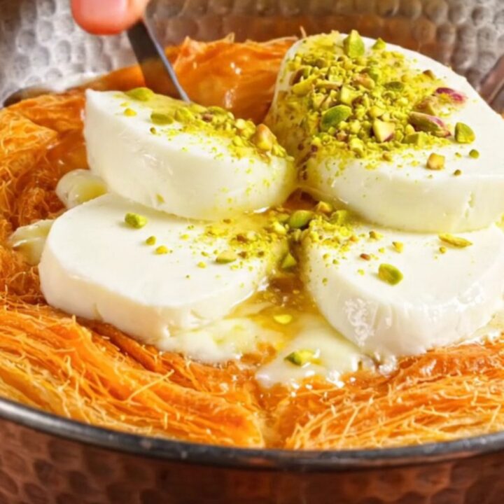 Freshly cooked pistachio kunefe in a copper pan, topped with ground pistachios and a glossy syrup