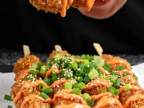 Crispy chicken skewers drizzled with sweet sriracha mayo on a black slate platter