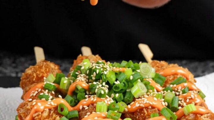 Crispy chicken skewers drizzled with sweet sriracha mayo on a black slate platter