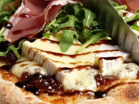 Caramelized onion and Brie flatbread with fig jam, prosciutto, and arugula on a baking sheet
