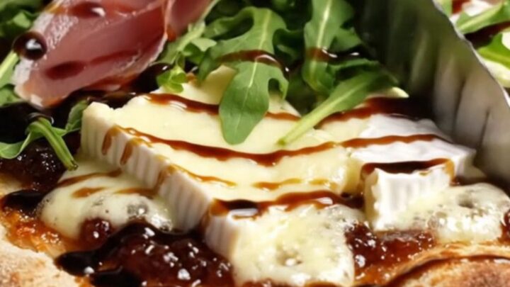 Caramelized onion and Brie flatbread with fig jam, prosciutto, and arugula on a baking sheet