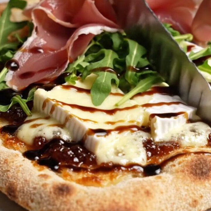 Caramelized onion and Brie flatbread with fig jam, prosciutto, and arugula on a baking sheet