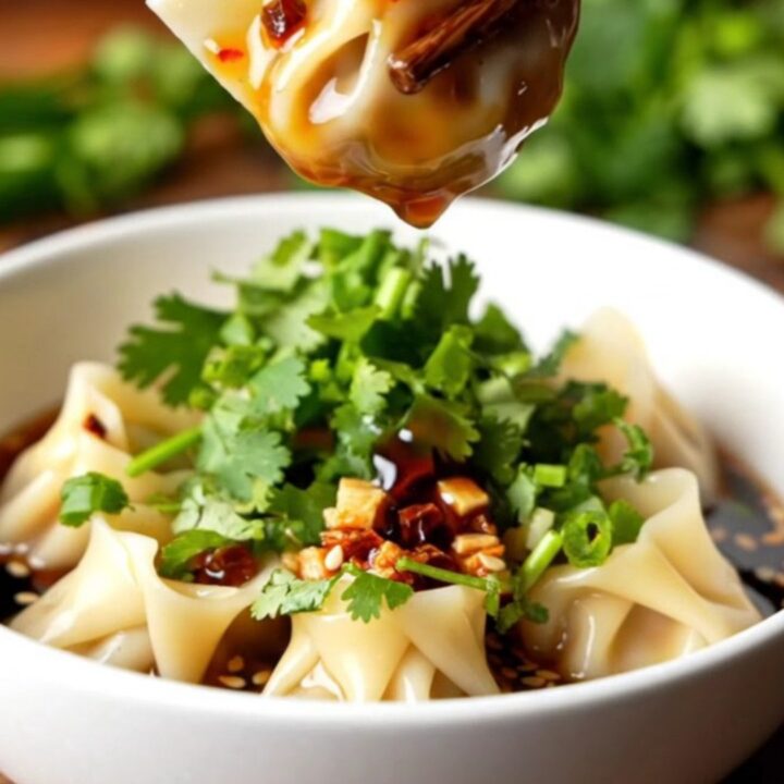 A bowl of Szechuan crispy chili oil dumplings with red sauce and cilantro garnish.